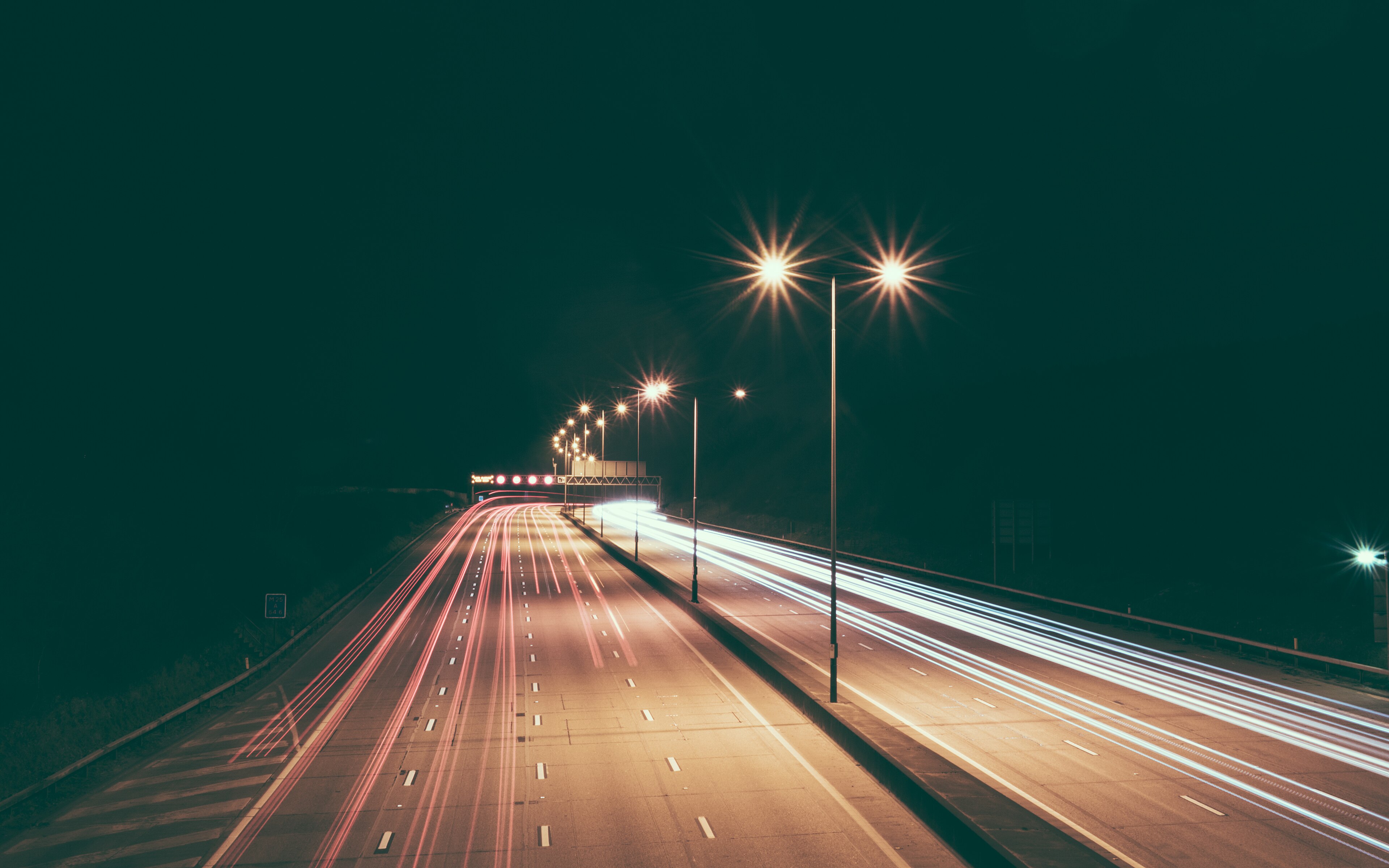 Eine mehrspurige Straße bei Nacht, die Lichter der Fahrzeuge als lange Spuren.